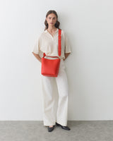 Person standing against a wall with a shoulder bag and hands in pockets.