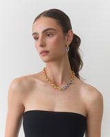 Person wearing a strapless top, gold and silver chain necklace, and hoop earrings.