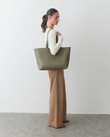 Person holding a large handbag and wearing a long-sleeve top with wide-legged pants.