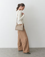 Person in a side pose holding a shoulder bag, wearing a sweater and wide-leg pants.
