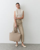 Person in sleeveless top and pants holding a large tote bag.
