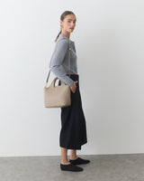 Person standing with shoulder bag, wearing a sweater and long skirt.