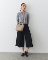 Person wearing cardigan, culottes, socks, and crossbody bag, standing against wall.