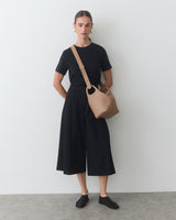 Person standing with a shoulder bag and wearing a T-shirt and wide-leg pants.