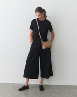 Person wearing a t-shirt and wide-legged pants with a crossbody bag.