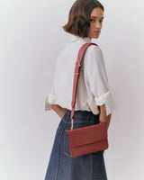 Person wearing a blouse and skirt, holding a shoulder bag.