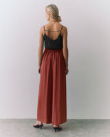 Person in a sleeveless top and long skirt standing on a plain background.