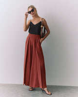 Person wearing sleeveless top and wide pants with sunglasses, holding a bag on shoulder.