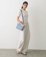 Person carrying a shoulder bag stands in a relaxed pose against plain background.