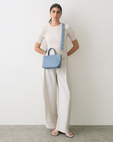 Person in wide-leg pants with shoulder bag, standing against plain wall.