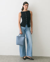 Person wearing a sleeveless top and wide-leg jeans holding a bag.