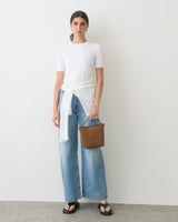 Person in jeans and t-shirt holding a small handbag, wearing sandals.