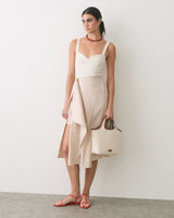 Person in a sleeveless top and layered skirt holding a handbag, wearing sandals.