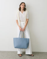 Person standing with a large tote bag, wearing a collared shirt and pants.