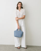 Person in white outfit holding a blue handbag.