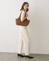 Person standing with shoulder bag, wearing long-sleeved top and pants with heels.