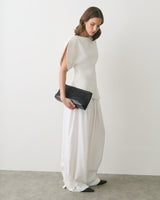 Person in a sleeveless top and wide pants holds a woven clutch