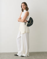 Model wearing a sleeveless top, long pants, and holding a fan with both arms crossed.
