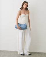 Person in strapless top and wide pants holding a handbag.