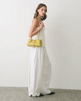 Person in sleeveless top and wide pants holding a small handbag.