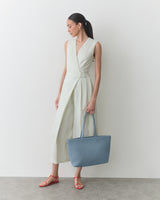 Person in sleeveless dress holds large handbag, stands in a relaxed pose.