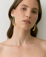 Person wearing long gold earrings with green accents