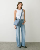 Person wearing a sleeveless top, jeans, holding a square bag with a strap across the chest.