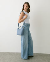Person standing with shoulder bag, wearing wide-leg jeans and sleeveless top.