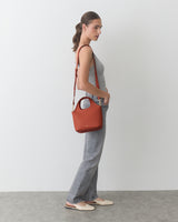 Person standing, wearing a sleeveless top, jeans, flats, holding shoulder bag.