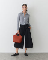 Person in buttoned shirt and wide-leg pants holding a handbag.