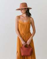 Person in dress and hat holding a handbag.