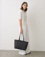 Person standing, holding a large handbag, wearing a short-sleeve top and wide-leg pants.