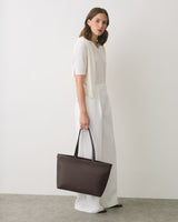 Person holding a large handbag stands against a plain background.