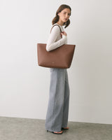 Woman standing, holding a large tote bag.