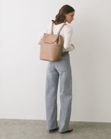 Person with backpack wearing long-sleeve shirt and jeans standing in a room.