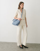 Person wearing light outfit with shoulder bag, standing on a plain background.
