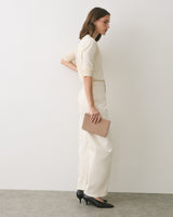 Person standing sideways holding a clutch purse, wearing long sleeve top and wide-leg pants.