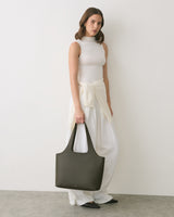 Woman in sleeveless top holding a large handbag, with a sweater tied around her waist.