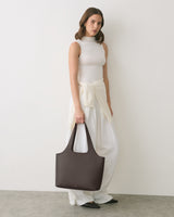 Woman in sleeveless top and wide pants holds a handbag.
