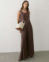 Person in sleeveless top and wide-leg pants holding a handbag.