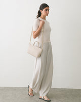 Person standing in profile, holding a shoulder bag, wearing loose-fitting pants and sandals.