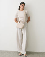 Person stands against wall, carrying a handbag, wearing a short-sleeve top and wide-leg pants.
