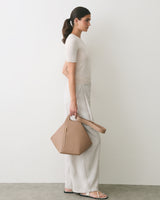 Person standing sideways holding a handbag wearing a short-sleeve top and pants.