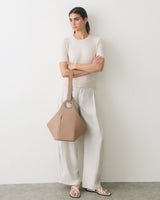 Person leaning on wall holding a geometric handbag, wearing a short-sleeve shirt and wide-leg pants.