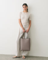 Person standing with a large handbag, wearing a short-sleeve shirt and wide-leg pants.