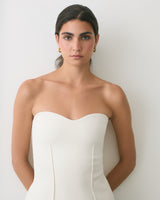 Person wearing a strapless dress and gold earrings standing against a plain backdrop.