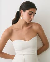 Person in strapless dress with earrings standing against a wall.
