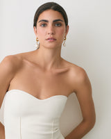 Person wearing a strapless top and earrings standing against a plain background.