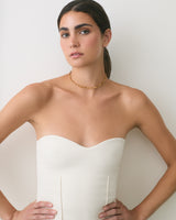 Person wearing strapless top and a necklace, leaning against a wall.