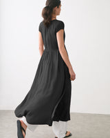 Person wearing a long dress with open back over pants standing indoors.
